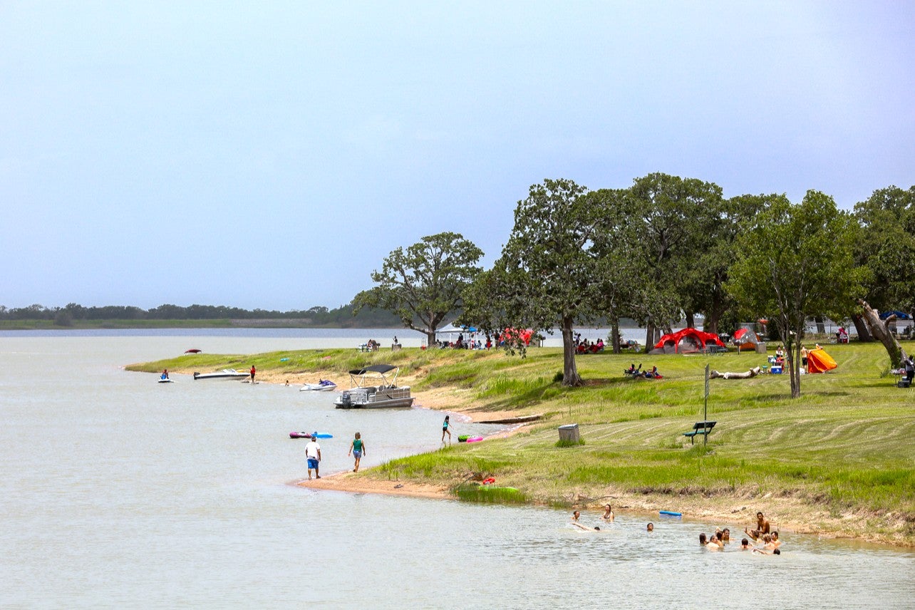 Visitors swimming, boating, and camping along the grassy shoreline at Lake Bryan