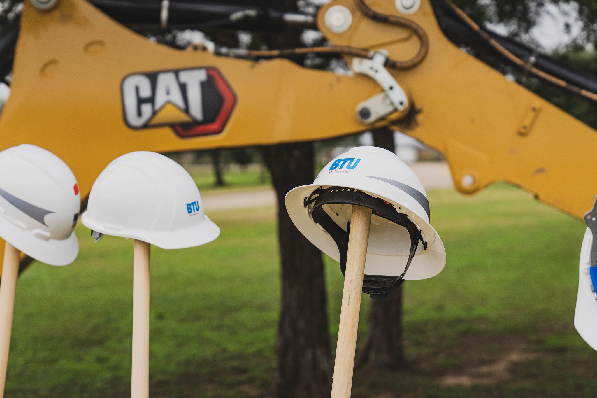 BTU hard hats on top of shovels in front of an excavator 